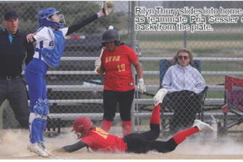 Rilyn Thury slides into home plate as teammate Pria Sessler steps back from the plate.