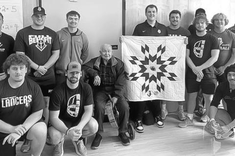 Sam Guest holding the Star Quilt presented to him alongside his team, Hunter Lhotak, and Elder Jerome Kills Small.